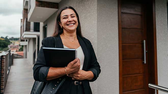 Mulher sorridente com pasta a entrar numa casa.